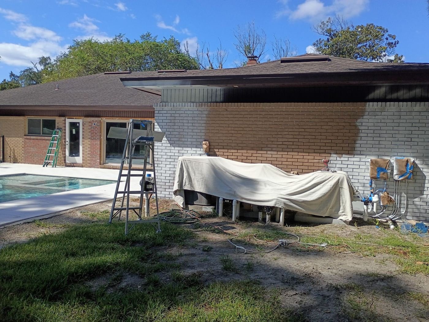 Brick pool house mid-repaint, equipment covered